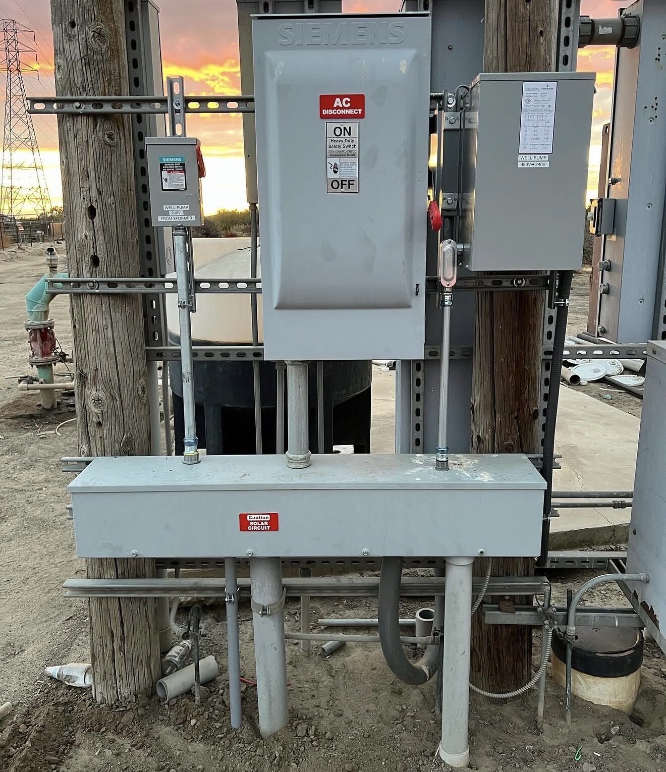 Full assembly — Siemens AC disconnect, well pump disconnect, and 480V to 240V transformer mounted on pole structure at sunset — Cyber Electric LLC