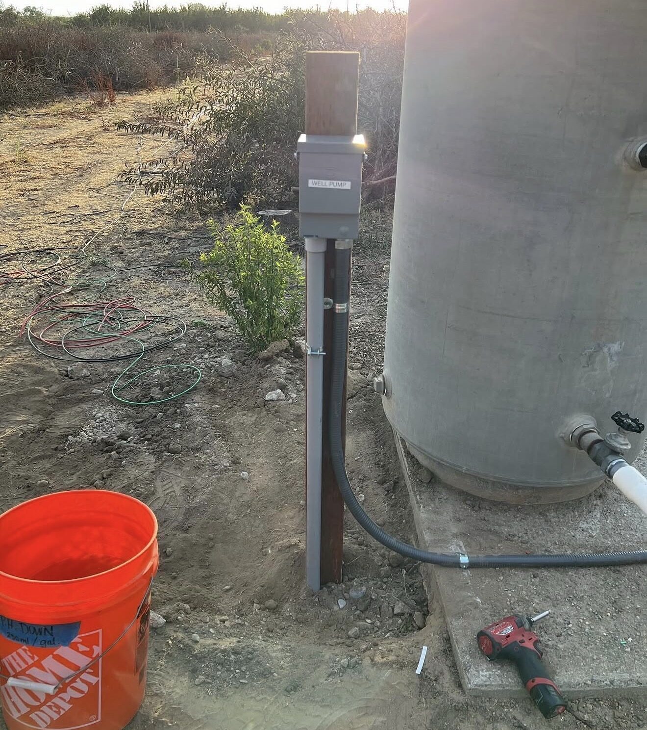 Well pump disconnect mounted on post next to concrete water tank in agricultural field — Cyber Electric LLC